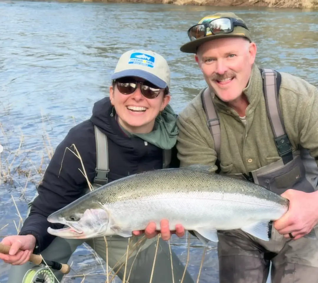 A couple fly fishing together with a trout
