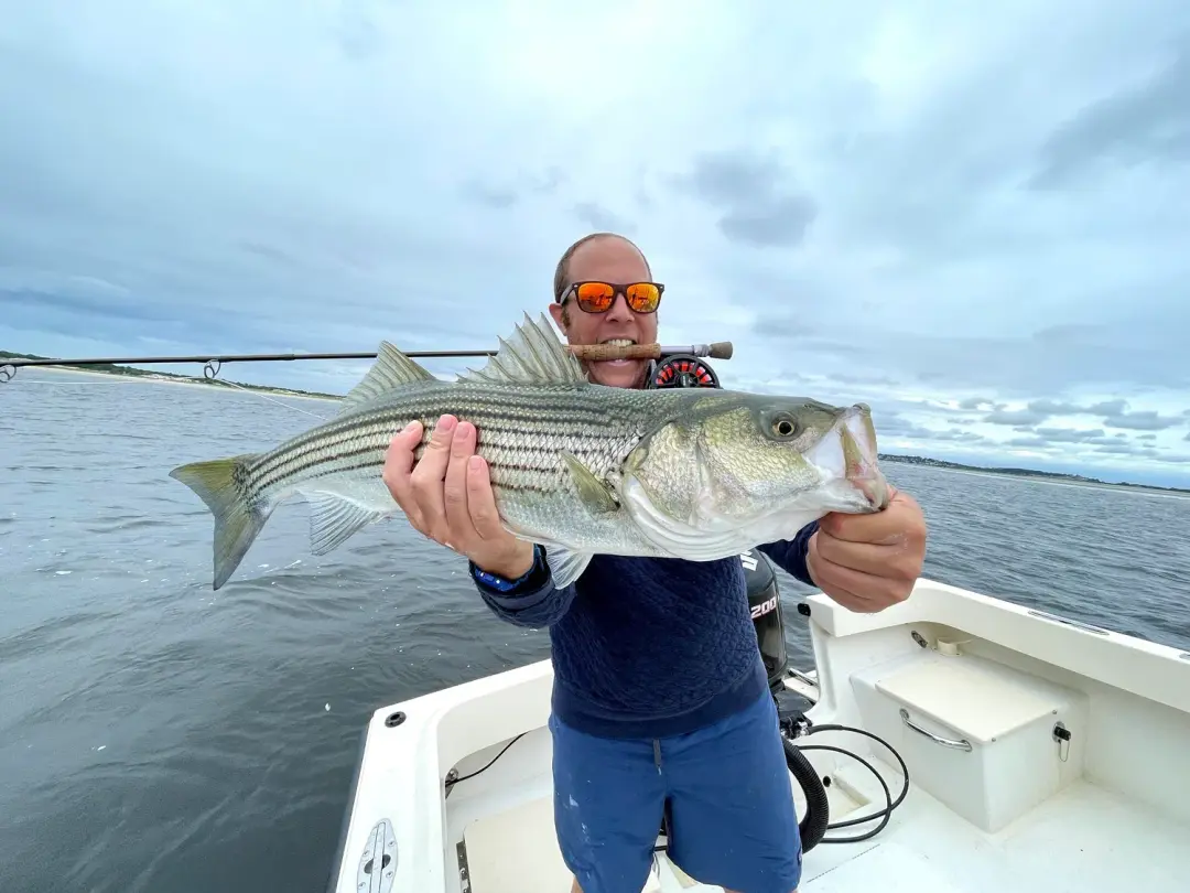 A striped bass held against a moody mountain lake